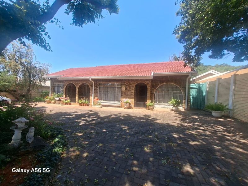 Front elevation of a single-story brick house featuring a tiled roof, paved driveway, and arched window detailing with security fixtures.