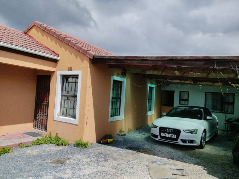 Front exterior view of the house featuring a covered carport, security gates, and window bars, showing signs of exterior wear.