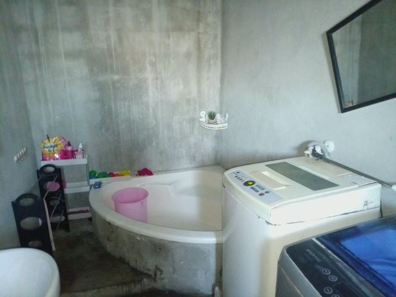 A bathroom space featuring a corner bathtub and unfinished concrete walls, requiring cosmetic finishing and renovation to improve functionality and aesthetic appeal.