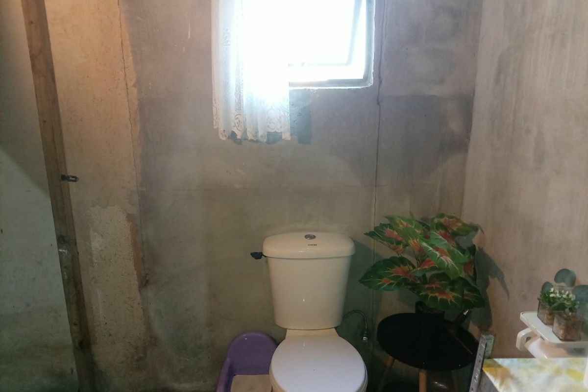 A functional bathroom space featuring a standard toilet and window, currently requiring wall finishing and cosmetic updates to improve the overall aesthetic.