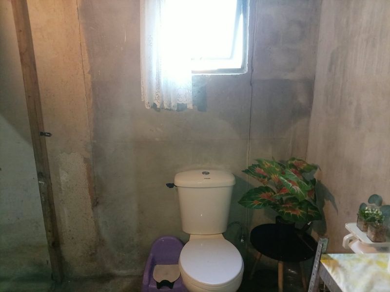 A functional bathroom space featuring a standard toilet and window, currently requiring wall finishing and cosmetic updates to improve the overall aesthetic.