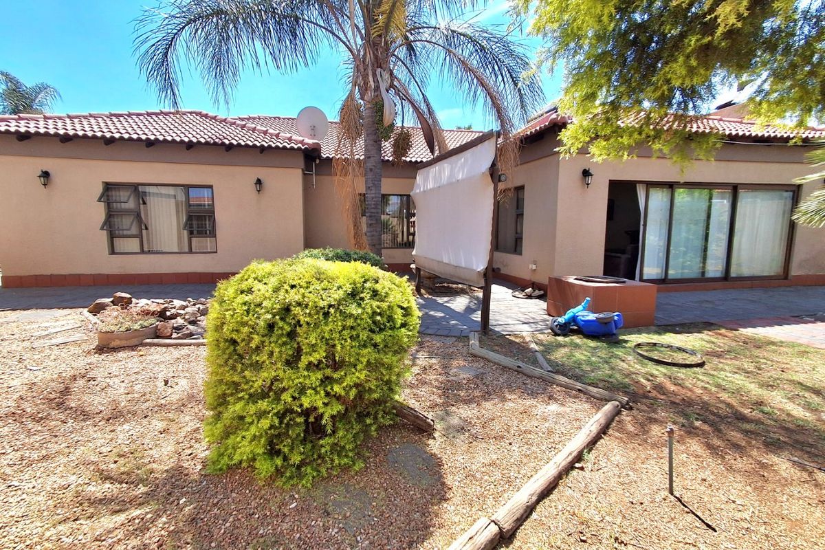 Rear view of the townhouse featuring a paved patio area, built-in braai, and sliding glass doors leading into the home.