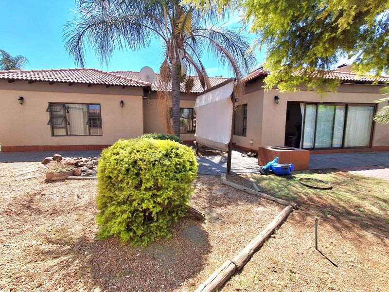 Rear view of the townhouse featuring a paved patio area, built-in braai, and sliding glass doors leading into the home.