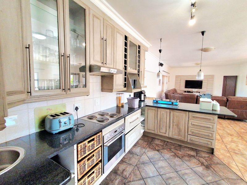 Spacious open-plan kitchen and living area featuring light wood cabinetry, granite countertops, integrated appliances, and tiled flooring throughout.
