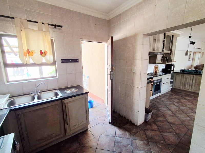 A functional scullery area featuring a double bowl sink, built-in cabinetry, and direct access to the exterior, providing additional prep and wash-up space.