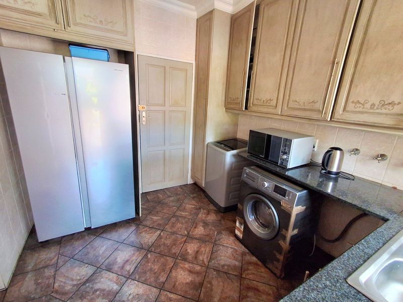 A functional scullery area featuring built-in cabinetry, granite countertops, and dedicated plumbing connections for laundry appliances.