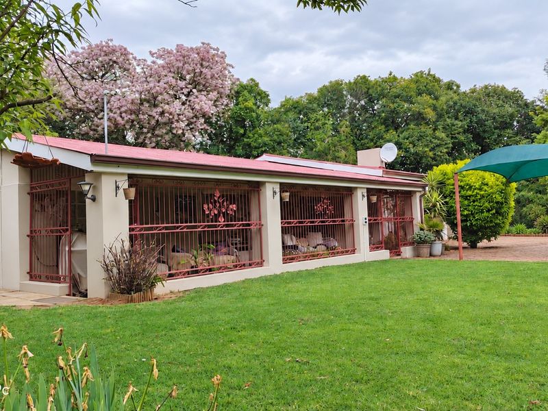 Rear view of the farm property featuring a covered patio area with security bars, a paved driveway, and a well-maintained lawn.