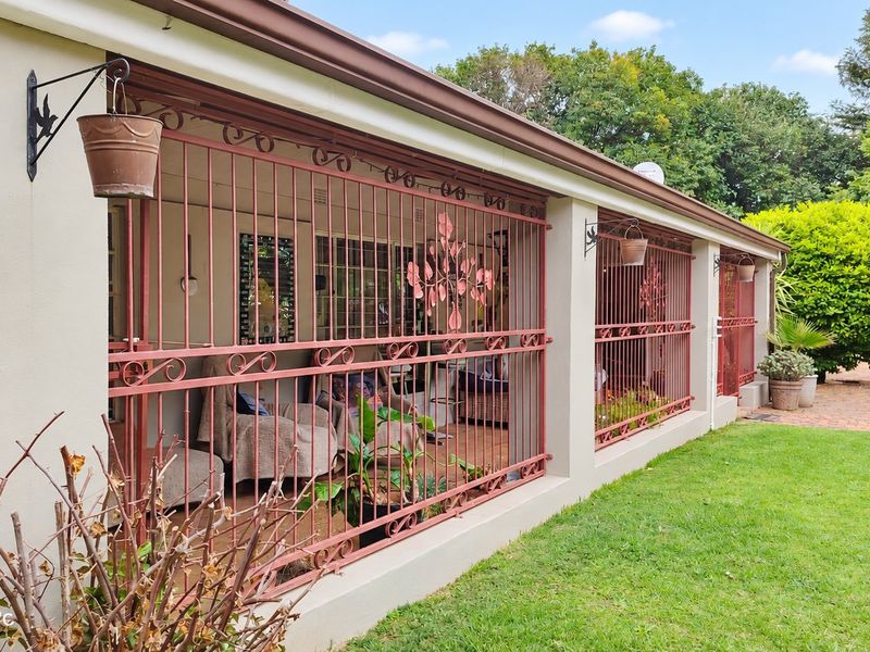 A covered patio area featuring decorative security bars, overlooking a well-maintained garden with brick paving and established greenery.