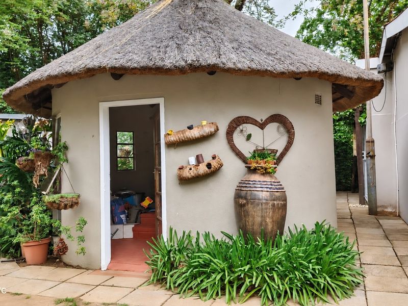 A charming circular structure with a traditional thatched roof, situated on a paved patio area within a garden setting.