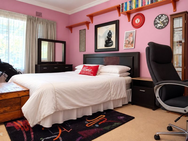 A bedroom featuring pink walls, built-in shelving, and a large window with curtains, providing a functional space with potential for modern updates.