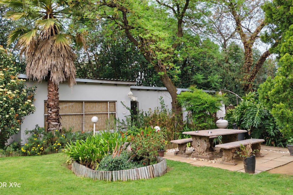 A private rear garden featuring a paved patio area with stone seating, mature trees, and established landscaping adjacent to the main dwelling.
