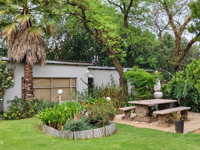 A private rear garden featuring a paved patio area with stone seating, mature trees, and established landscaping adjacent to the main dwelling.