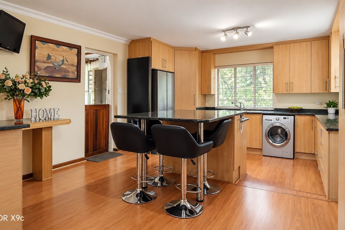 A well-maintained kitchen featuring light wood cabinetry, granite countertops, integrated laundry appliances, and durable laminate flooring with a functional breakfast bar layout.