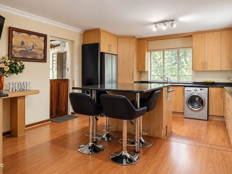 A well-maintained kitchen featuring light wood cabinetry, granite countertops, integrated laundry appliances, and durable laminate flooring with a functional breakfast bar layout.