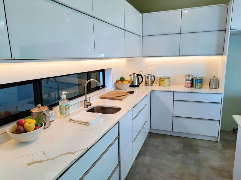 Modern kitchen featuring high-gloss white cabinetry, stone countertops, integrated under-cabinet lighting, and a sleek horizontal window backsplash.