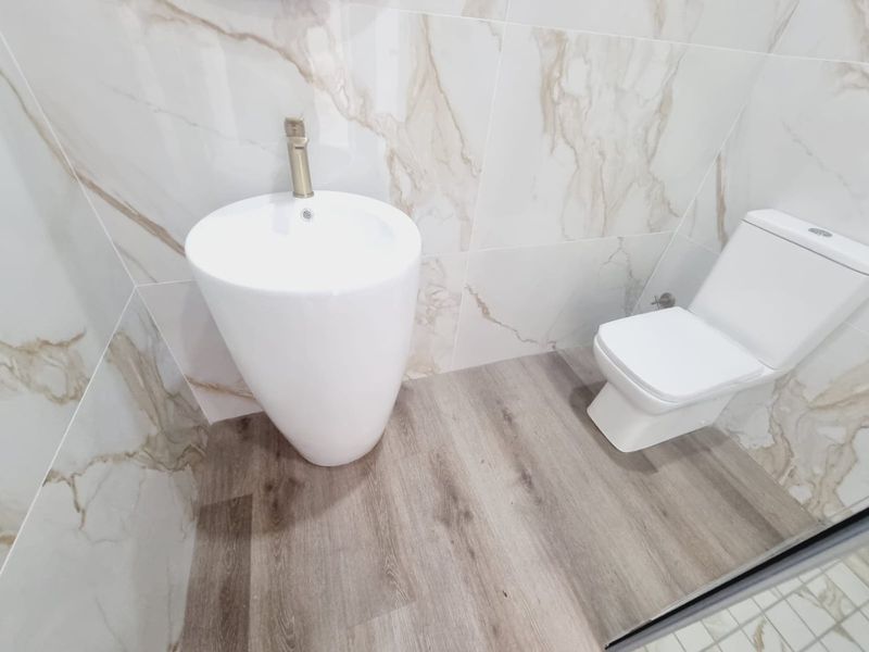 A modern, minimalist bathroom featuring a sleek pedestal basin with brass faucet, a contemporary toilet, and elegant marble-look wall tiles.