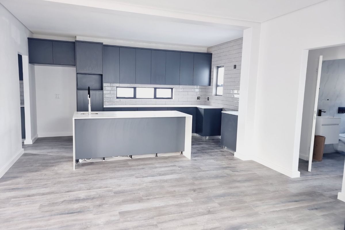Modern open-plan kitchen featuring dark grey cabinetry, white countertops, subway tile backsplash, and light wood-look laminate flooring in a newly finished space.