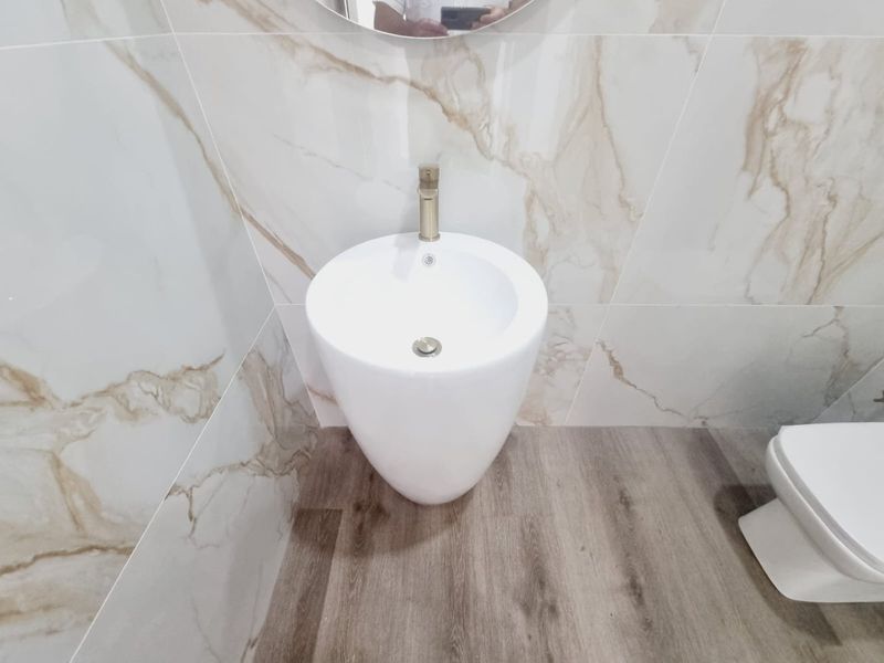 Modern bathroom featuring a sleek freestanding basin with brass tapware, complemented by elegant marble-look wall tiles and wood-look flooring.
