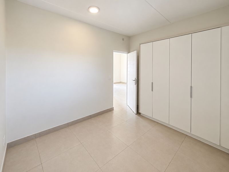 A bright, empty bedroom featuring neutral tiled flooring and ample built-in cupboard storage, offering a clean and versatile space.