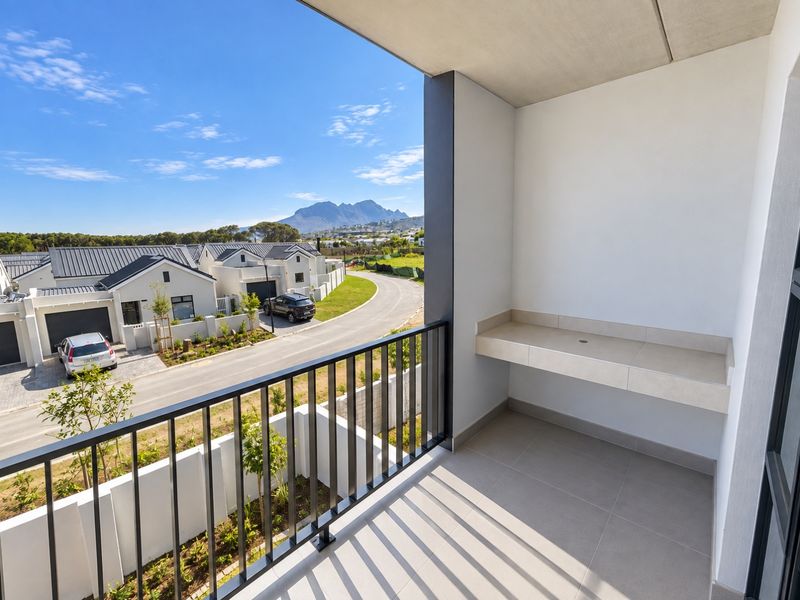 A modern balcony featuring a built-in stone counter, metal balustrade, and tiled flooring, offering scenic views of the surrounding residential estate and mountains.