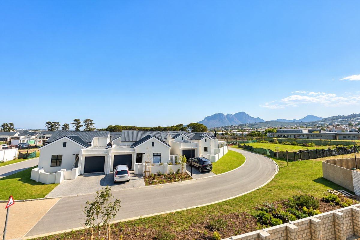 An elevated aerial view of a modern residential complex featuring white facades, metal roofing, paved driveways, and well-maintained lawns with mountain views.