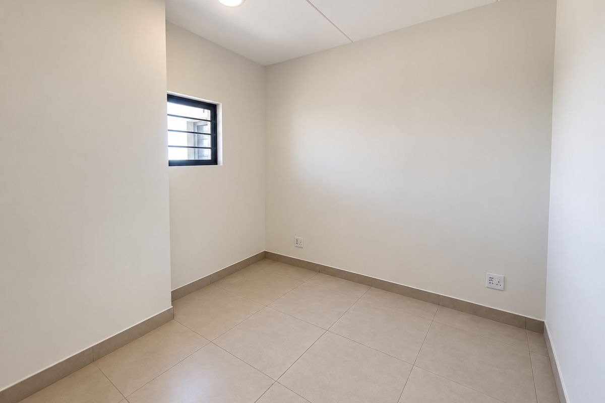 A clean, empty bedroom featuring neutral tiled flooring, a small window with security bars, and modern electrical finishes.