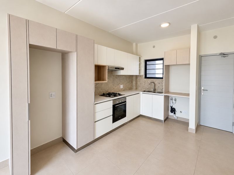 Modern, clean-lined kitchen featuring built-in cabinetry, integrated gas hob, electric oven, extractor fan, and neutral tiled flooring in an open-plan layout.