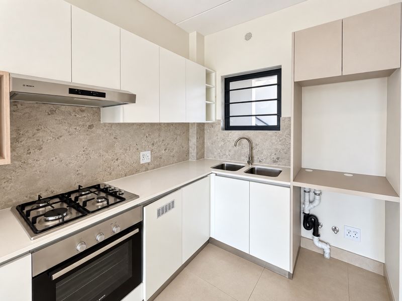 Modern kitchen featuring white cabinetry, stone countertops, gas hob, built-in oven, extractor fan, and dedicated plumbing for appliances.