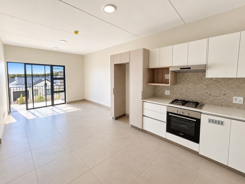 Modern open-plan kitchen and living area featuring sleek cabinetry, integrated appliances, tiled flooring, and a sliding door leading to a private balcony.