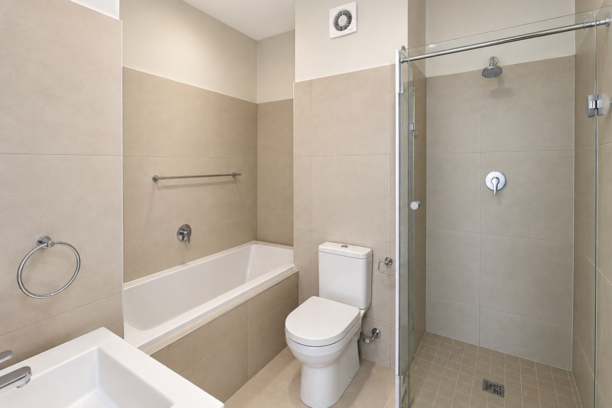 Modern bathroom featuring a built-in bathtub, separate glass-enclosed shower, toilet, and neutral floor-to-ceiling tiling.