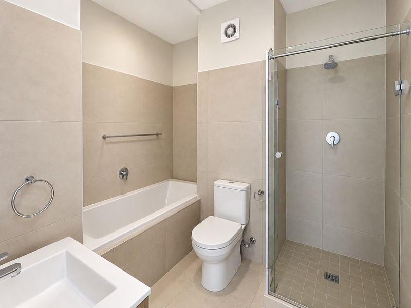 Modern bathroom featuring a built-in bathtub, separate glass-enclosed shower, toilet, and neutral floor-to-ceiling tiling.