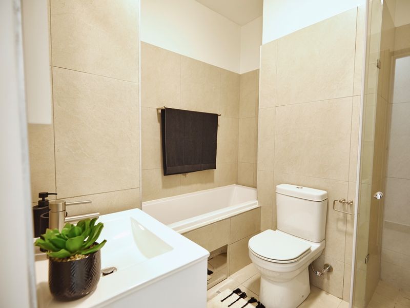 Modern bathroom featuring a built-in bathtub, toilet, vanity basin, and a glass-enclosed shower area with neutral wall tiling.