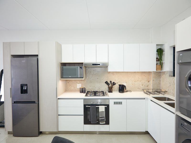 Modern kitchen featuring sleek white cabinetry, stone splashback, integrated gas hob, electric oven, and built-in microwave with high-quality finishes.