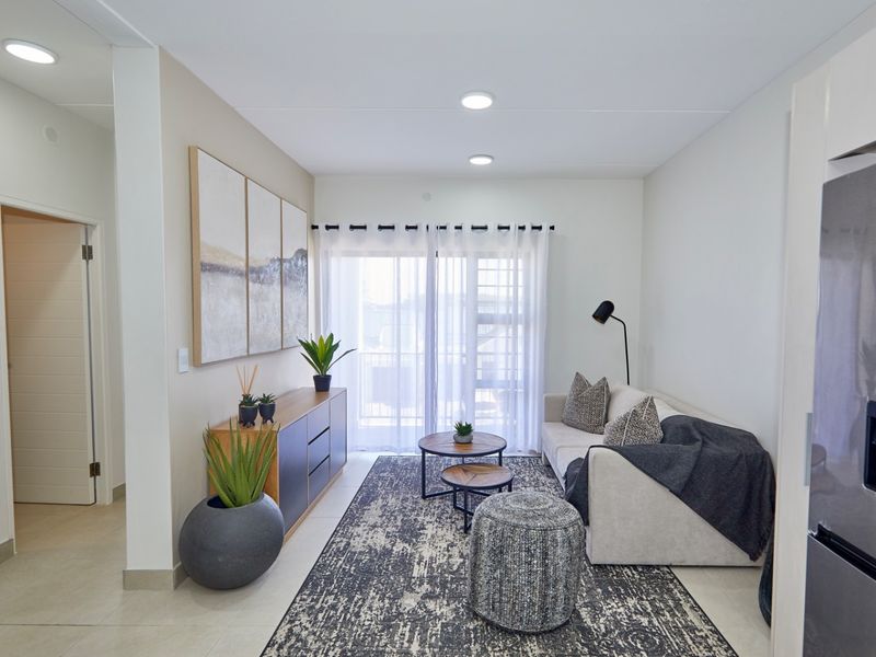 A bright and modern living room featuring tiled flooring, recessed ceiling lighting, and a sliding glass door providing access to the outdoor area.