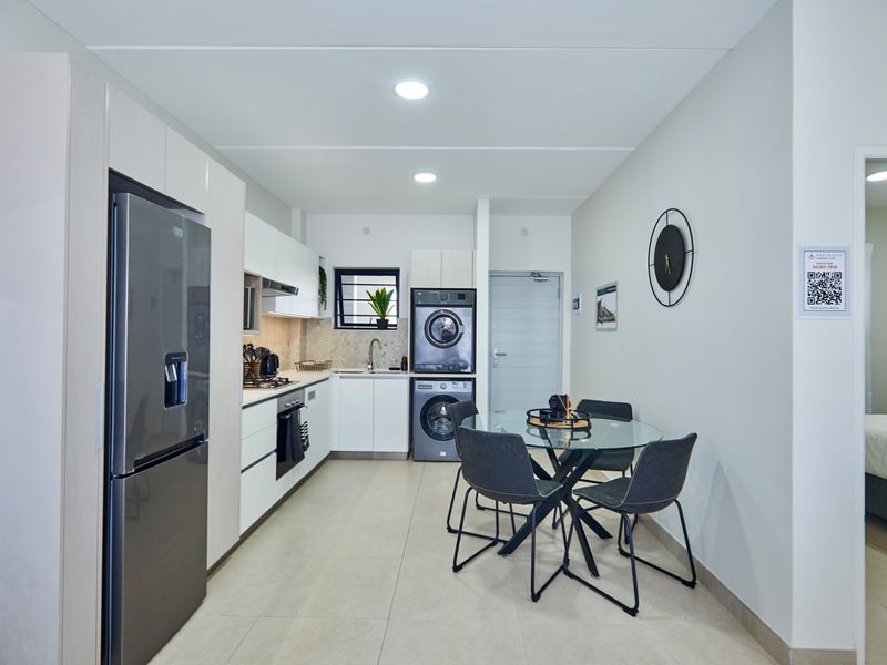 Modern open-plan kitchen and dining area featuring sleek cabinetry, integrated appliances, tiled flooring, and recessed lighting, creating a clean and functional living space.