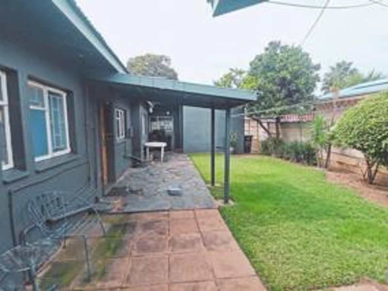 Rear exterior view featuring a covered patio area, paved walkway, and a well-maintained lawn with boundary walling.