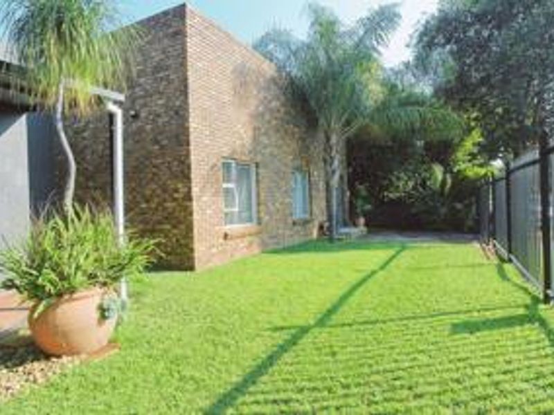 A well-maintained rear garden featuring a face brick exterior wall, a paved patio area, and secure metal perimeter fencing.