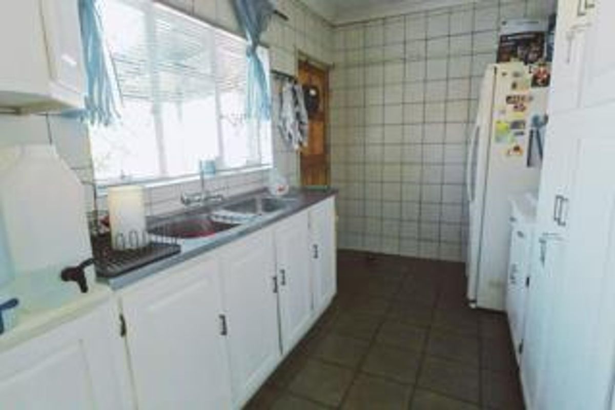 A functional kitchen featuring white built-in cabinetry, tiled splashbacks, and tiled flooring, offering a practical layout with ample storage space.