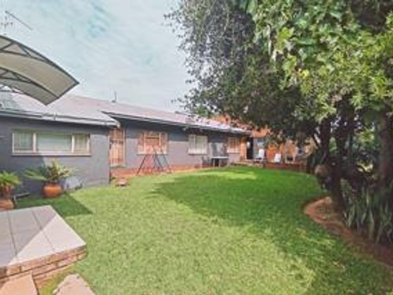 A view of the rear garden featuring a small tiled patio with an awning, a well-maintained lawn, and mature trees.