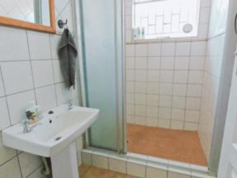 Functional bathroom featuring a pedestal washbasin and a glass-enclosed shower with tiled walls and security bars on the window.