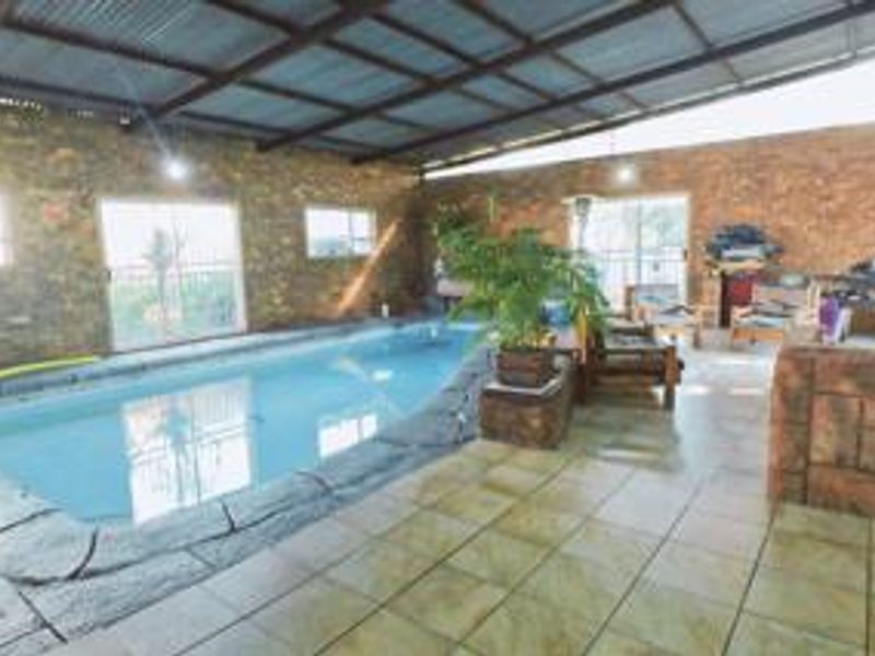 An indoor swimming pool area featuring stone-clad walls, tiled flooring, and a high corrugated metal roof with large sliding glass doors.