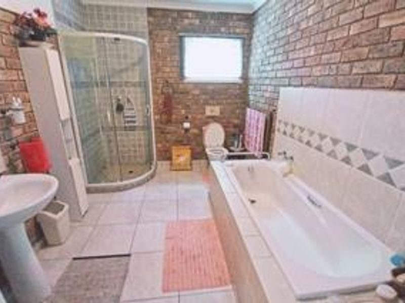 A functional bathroom featuring a corner shower, built-in bathtub, pedestal basin, and toilet, finished with exposed brick walls and tiled flooring.