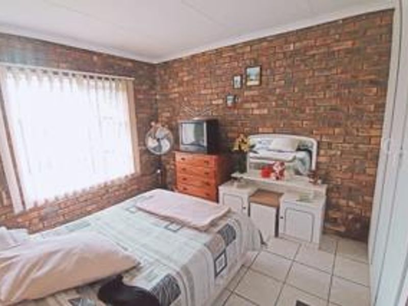 A bedroom featuring an exposed brick feature wall, tiled flooring, and built-in wardrobe storage.