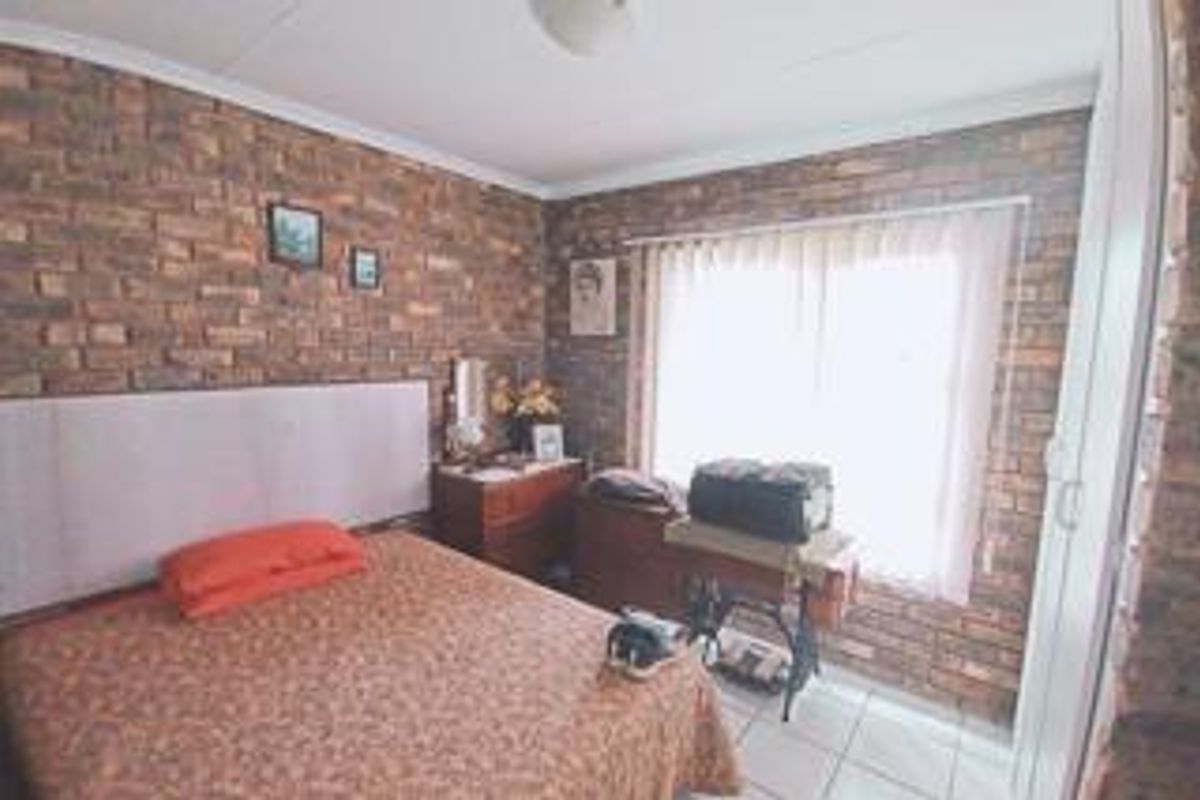 A bedroom featuring exposed brick walls, tiled flooring, and a built-in cupboard, offering a rustic aesthetic with natural light from the window.