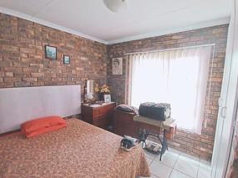A bedroom featuring exposed brick walls, tiled flooring, and a built-in cupboard, offering a rustic aesthetic with natural light from the window.