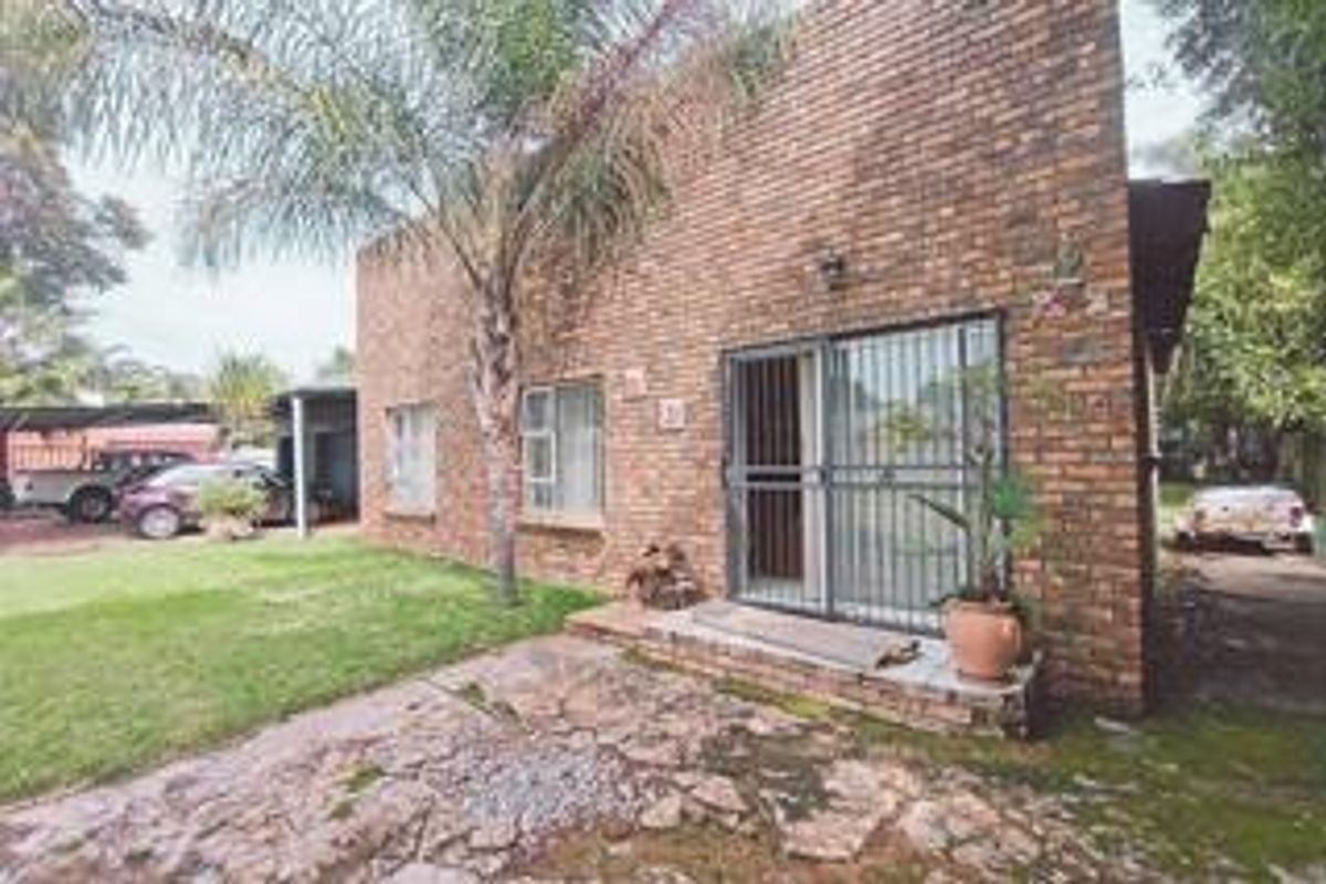 Rear view of the property featuring an exposed brick facade, sliding glass door with security gate, and a stone paved patio area.