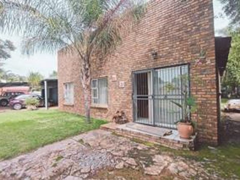 Rear view of the property featuring an exposed brick facade, sliding glass door with security gate, and a stone paved patio area.