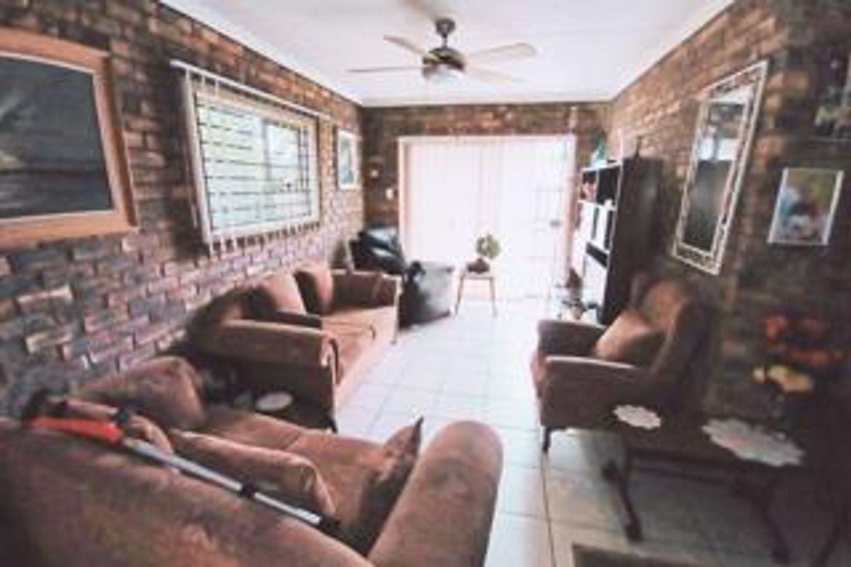 A living room featuring exposed brick walls, tiled flooring, a ceiling fan, and a sliding glass door providing access to the exterior.