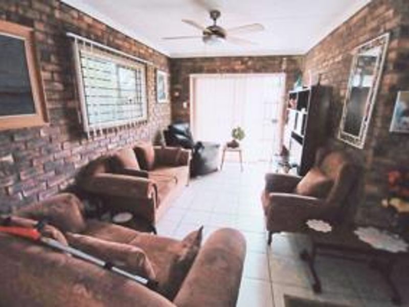 A living room featuring exposed brick walls, tiled flooring, a ceiling fan, and a sliding glass door providing access to the exterior.