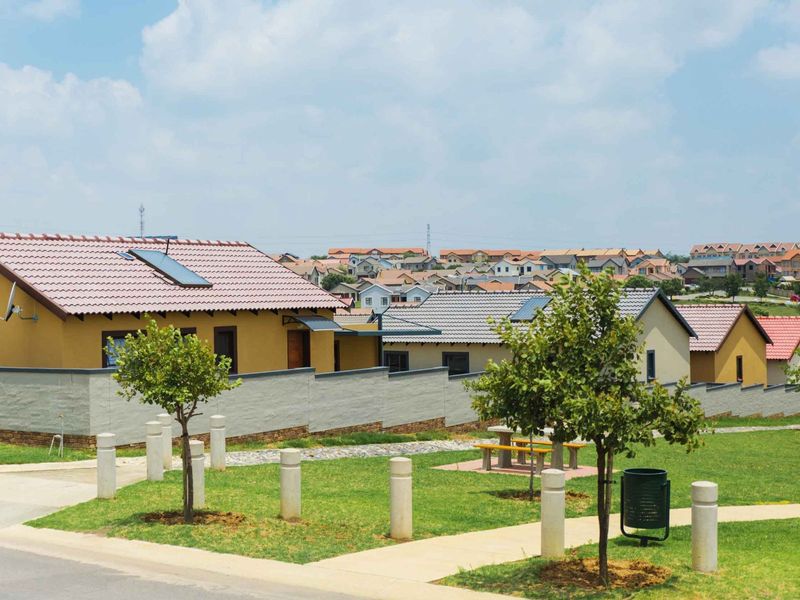 A view of a residential street featuring well-maintained homes with tiled roofs, solar water heaters, and landscaped communal green spaces.